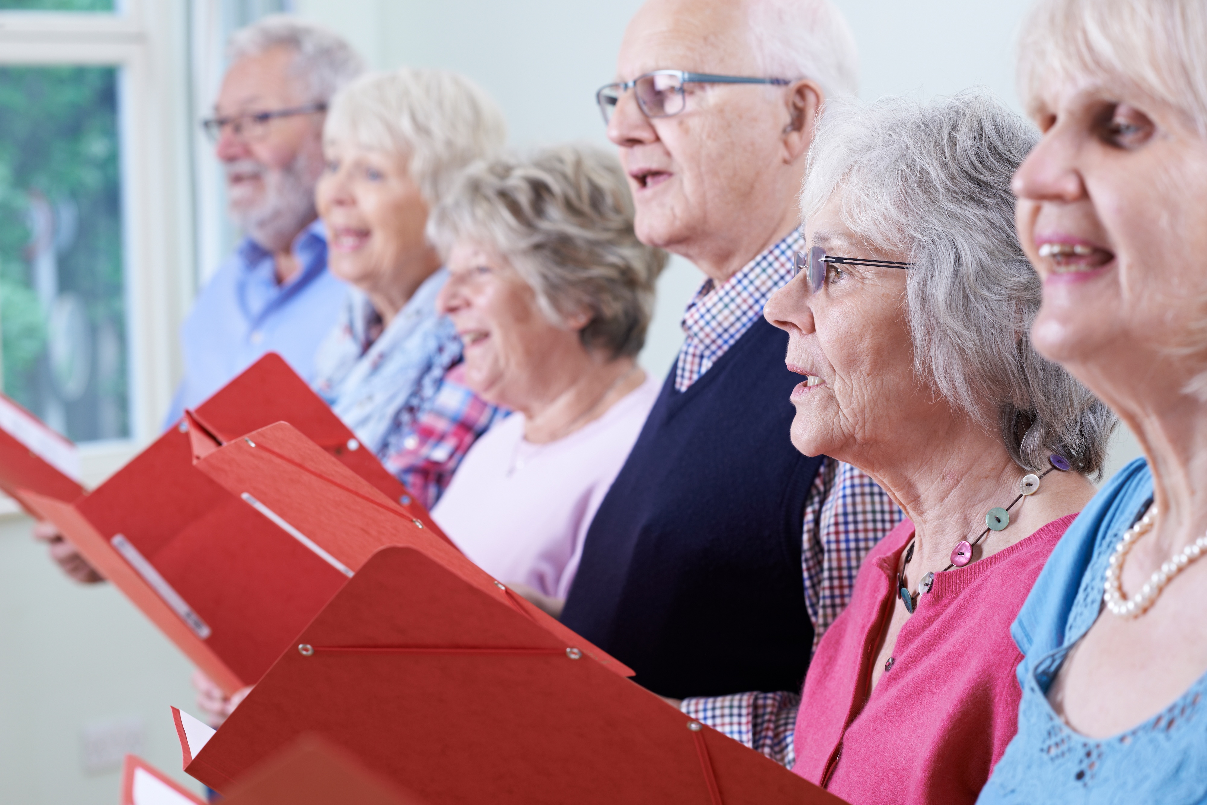 Mitglieder eines Gesangsvereins stehen in einer Reihe und singen gemeinsam aus roten Notenmappen.
